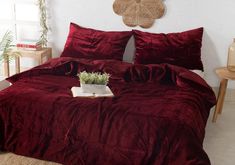 a bed with red comforter and pillows in a white room next to a potted plant