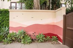 a wall painted with birds and plants on the side of a building next to a gate