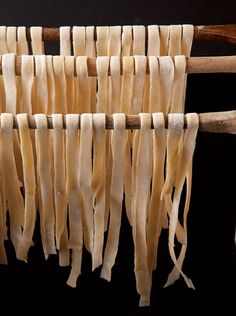 several pieces of pasta hanging from a wooden hanger on a black background with space for text