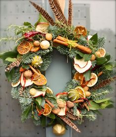 a christmas wreath with oranges, cinnamons and other holiday decorations hanging on a door