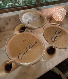 three glasses filled with liquid sitting on top of a marble counter next to a window