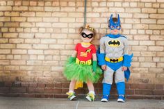 two little kids dressed up as batman and robin wayne standing in front of a brick wall