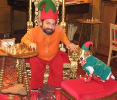 a man in an orange shirt and red pants sitting on a chair with a dog