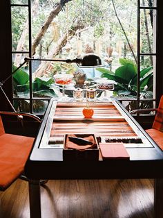 a dining room table with orange chairs and an open window