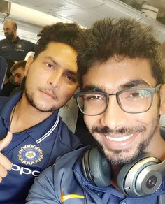 two men sitting on an airplane with headphones around their necks and one pointing at the camera