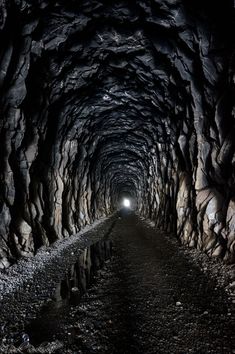 a dark tunnel with light at the end and rocks on both sides leading into it