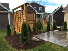 a backyard with landscaping and trees in the front yard, including a pergolated trellis