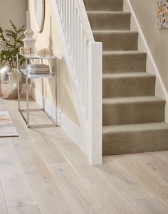 a white staircase with beige carpet and wooden flooring next to a mirror on the wall