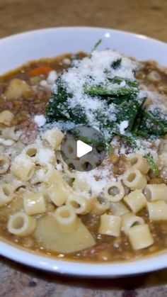 a white bowl filled with pasta and cheese on top of a wooden table next to a spoon