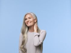 a woman with long blonde hair smiling and holding her hand to her ear, against a blue background