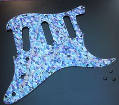 a blue and purple guitar pickguard with holes in the bottom half, on a black surface