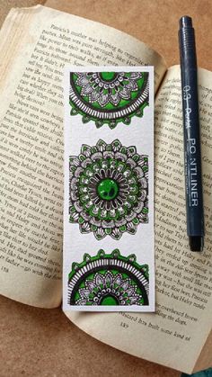 an open book with green and white designs on it next to a black marker pen