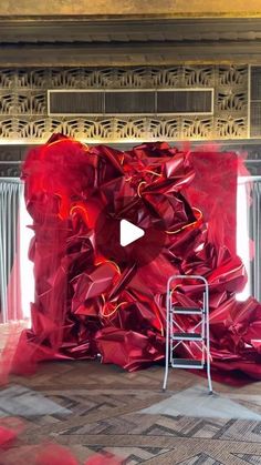 a large red piece of art sitting on top of a floor next to a ladder