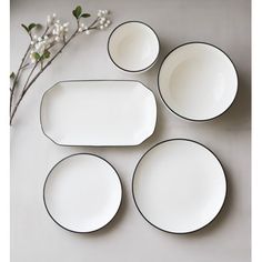 four white plates with black rims on a gray surface next to a flower branch