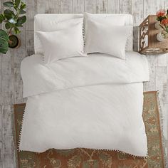 a bed with white sheets and pillows on top of a rug next to a potted plant