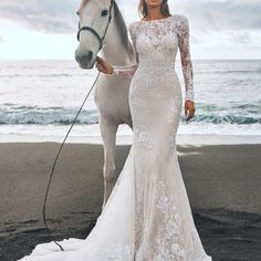 a woman standing next to a white horse near the ocean