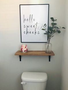 a white toilet sitting next to a wooden shelf with a plant on top of it