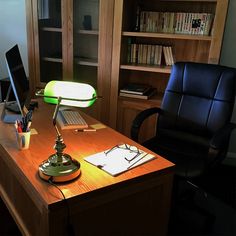 an office desk with a laptop computer on top of it next to a chair and bookshelf