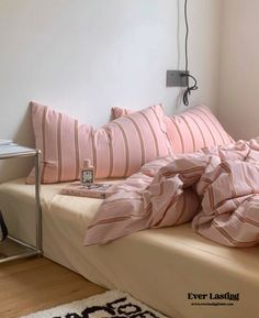 an unmade bed with pink and white striped pillows on it, next to a small table