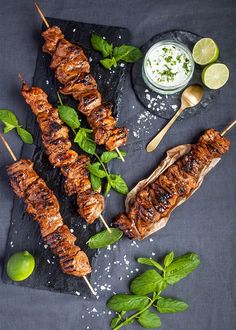 several skewers of meat and vegetables on a slate platter with limes