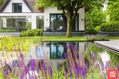 the house is surrounded by lush green trees and purple flowers on the water's edge