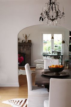 a dining room table with white chairs and a bowl of fruit on top of it