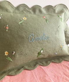 two green pillows with embroidered name and flower designs on them sitting on a pink bed