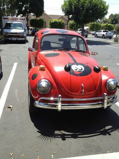 an old red car with a face painted on it's side in a parking lot