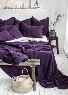 a bed with purple sheets and pillows in a room next to a wooden bench on the floor