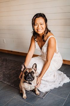 a woman kneeling down next to a small pug dog on a rug in front of a white wall