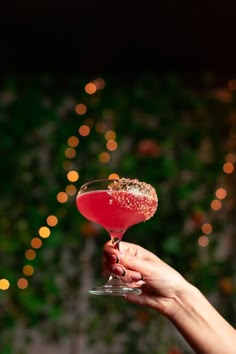 a hand holding a wine glass filled with red liquid and sprinkled with gold flakes