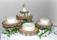 a table topped with three cakes covered in white frosting and surrounded by greenery