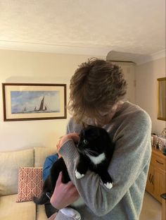 a woman holding a black and white cat while sitting on top of a couch in a living room