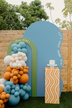 an outdoor party with balloons and cake on the grass in front of a wooden fence