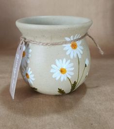 a white flower pot with daisies painted on it and a tag hanging from the handle