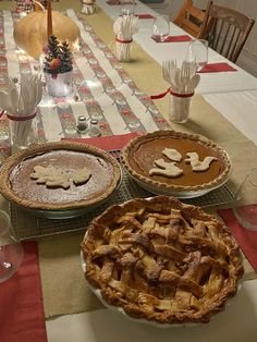 three pies sitting on top of a table covered in plates and glasses next to each other