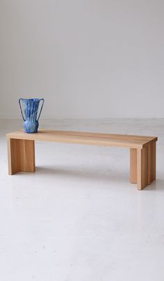 a blue vase sitting on top of a wooden bench in front of a white wall