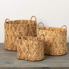 three woven baskets sitting on top of a wooden table next to each other with handles