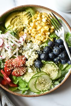 a salad with blueberries, cucumbers, tomatoes and other toppings in a bowl