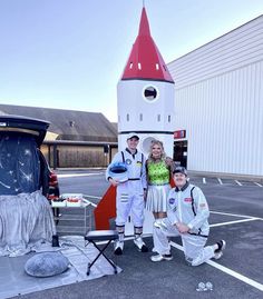 three people standing in front of a rocket ship