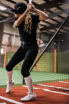 a woman holding a baseball bat on top of a batting cage at a ball park