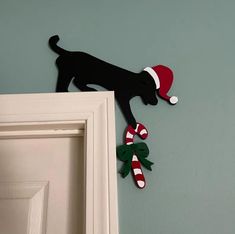 a black dog with a santa hat and candy canes hanging on the wall next to a door