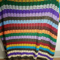 a multicolored crocheted blanket hanging on a wall