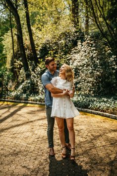 a man holding a woman in his arms while standing on the ground surrounded by trees