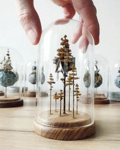 a hand is touching a glass dome with trees inside it on a wooden table next to other small houses