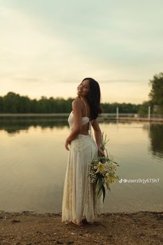 a woman in a white dress is standing by the water