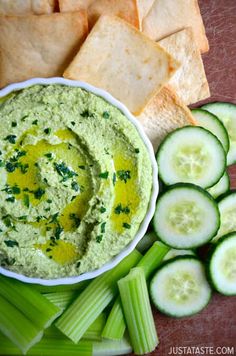 cucumber and crackers are arranged on a cutting board with dip in the middle