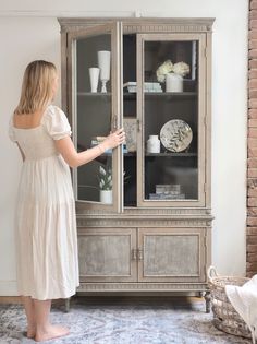 a woman standing in front of a china cabinet