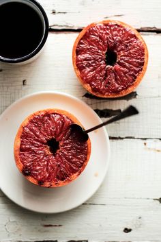 two blood orange halves on a white plate next to a cup of coffee and spoon