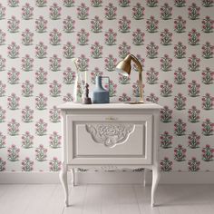 a white dresser with pink flowers on the wall next to it and a lamp in front of it